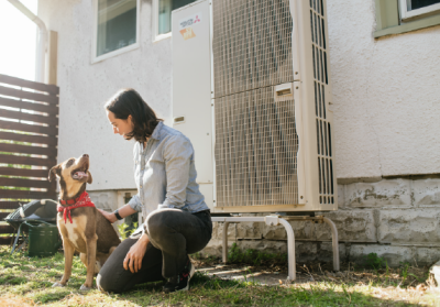 homeowner kneeling next to outdoor heat pump unit with dog